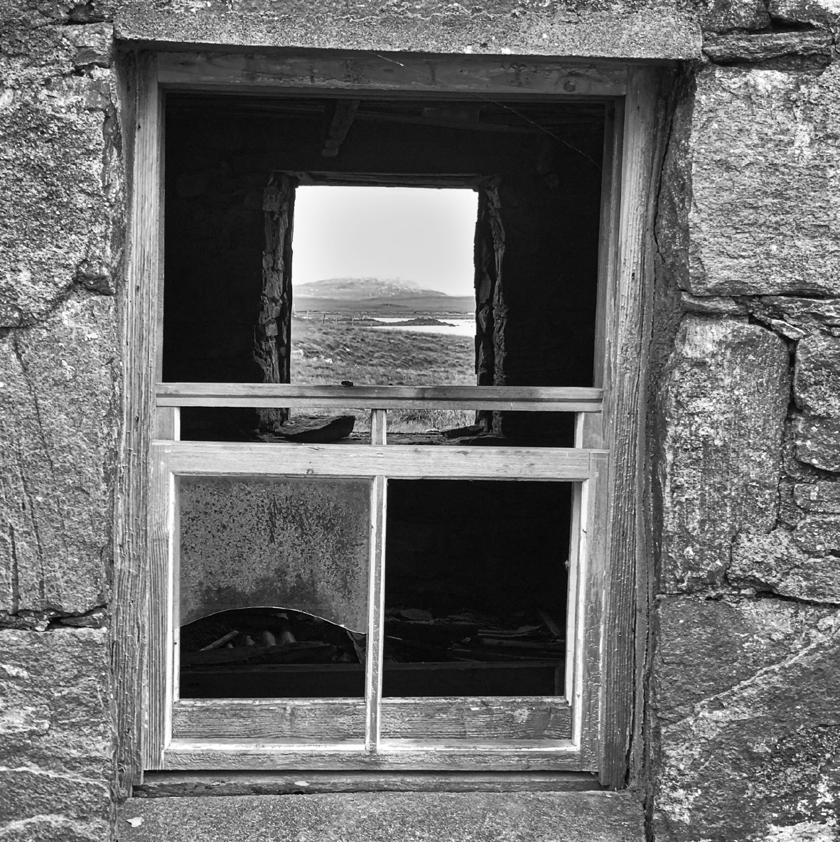 Black & White image of a window in a stone property through which can be seen lanscape beyond.